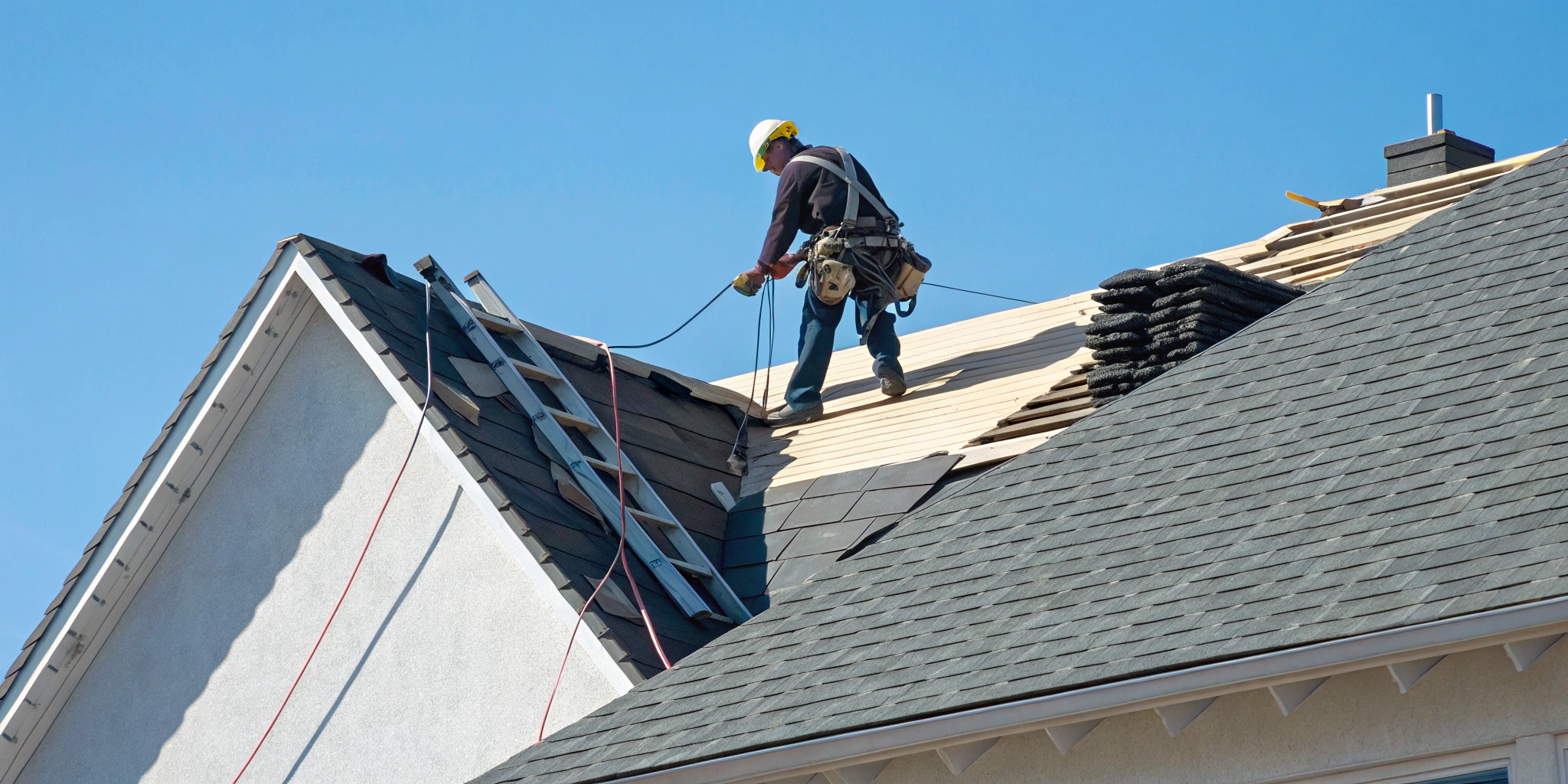 Commercial roofing contractor repairing a business roof with shingles and safety gear.